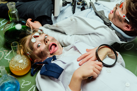 side view of kids in lab coats lying on chalkboard after experiment magnifying glassの写真素材