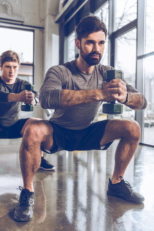 young men in sportswear with dumbbells exercising at the gymの写真素材