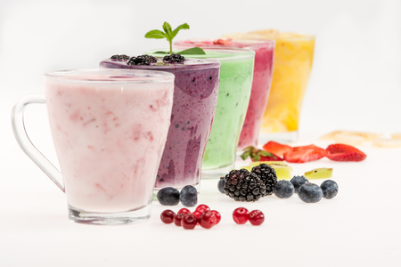Close-up view of fresh fruit smoothies in glass cups isolated on whiteの写真素材