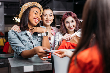 Happy stylish young women paying with credit card in shopping mallの写真素材