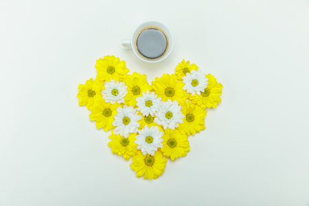 Top view of beautiful white and yellow chrysanthemum flowers in heart shape and cup of coffee isolated on whiteの写真素材
