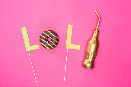 Food composition concept with donut in chocolate glaze and golden bottle isolated on pinkの写真素材