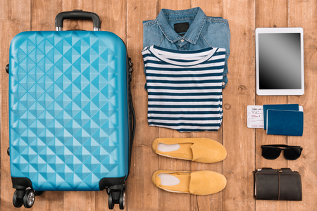 Flat lay with luggage, male clothes, accessories and digital tablet on wooden floor. Ready for travel conceptの写真素材