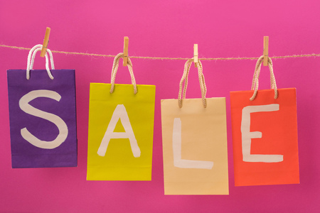 colorful sale signs on shopping bags hanging on rope isolated on pink, offer sale tagsの写真素材