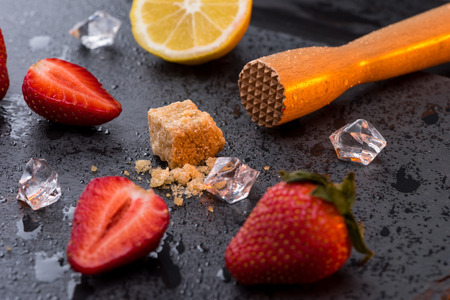 wooden squeezer with lemon and strawberries slices on stone board, barman cocktail
