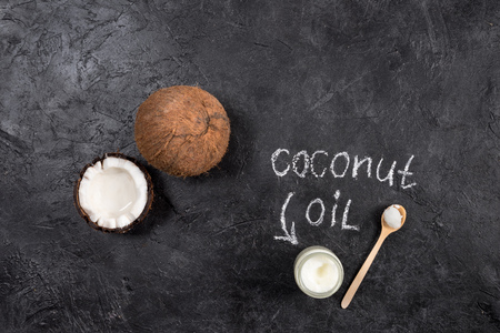 Top view of coconut oil in glass jar with spoon and cracked coconut on blackの写真素材