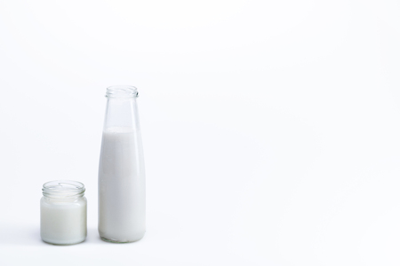 organic coconut oil in glass jar and coconut milk in glass bottle isolated on white, coconut drink conceptの写真素材