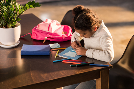 Adorable little girl sitting at table and drawing with colorful felt tip pensの写真素材