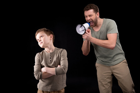 Father with megaphone screaming at son standing with crossed arms and looking awayの写真素材