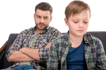 Serious father with crossed arms looking at upset little boyの写真素材