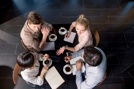 Overhead view of young businesspeople discussing project at table with cups of coffeeの写真素材
