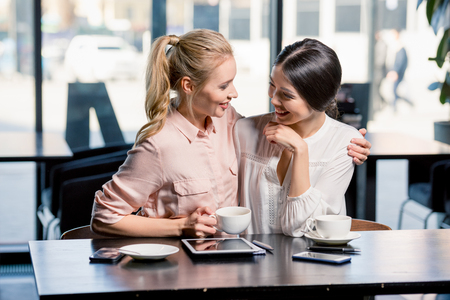 Smiling young women using digital tablet while drinking coffee in cafeの写真素材