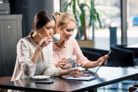 Smiling young women using digital tablet while drinking coffee in cafeの写真素材