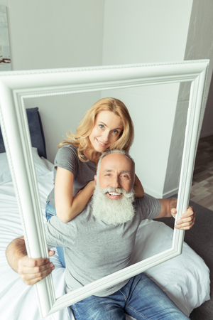 middle aged couple sitting on bed with picture frameの写真素材