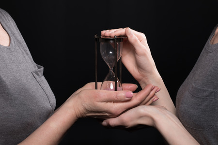 woman giving hourglass to his daughter isolated on blackの写真素材