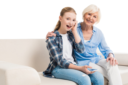 grandmother and grandchild listening music and sitting on sofaの写真素材