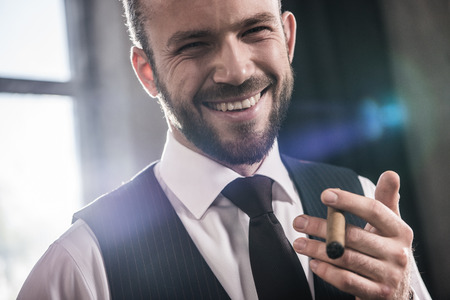 handsome smiling confident man smoking cigar indoorsの写真素材