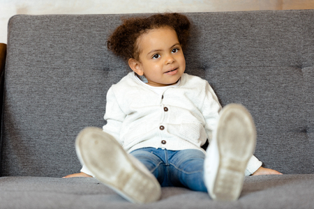 little african american girl sitting on sofa at homeの写真素材