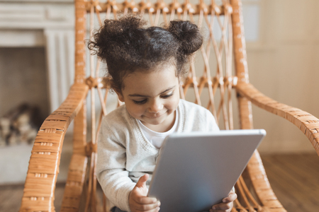 little african american girl using digital tablet and sitting on rocking chair at homeの写真素材