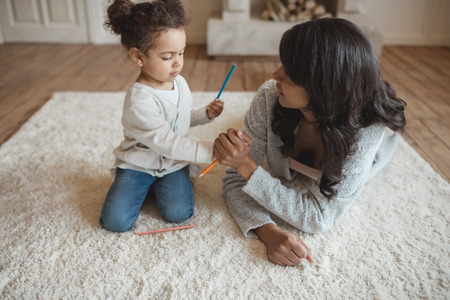 african american mother sitting on floor with adorable little daughter holding pencilsの写真素材