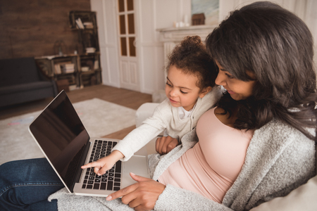 Mother using laptop and cute little daughter pointing at blank screenの写真素材