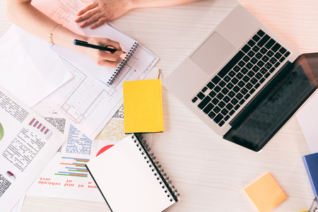 cropped shot of businesswoman writing with pen at workplace on tabletop with laptopの写真素材