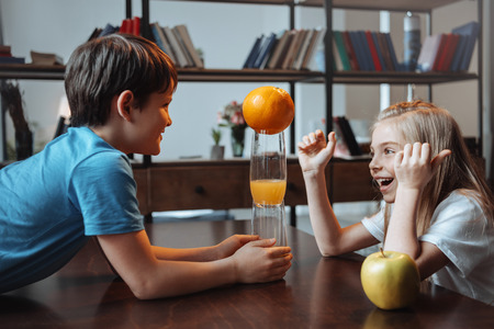 boy and girl playing with glasses and fruits at kitchen togetherの写真素材