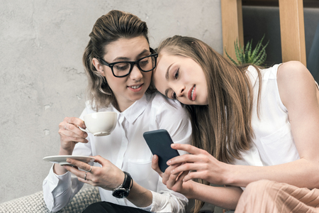 lesbian couple drinking coffee and using smartphone togetherの写真素材