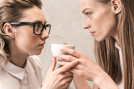 beautiful young women holding coffee cup and looking at each otherの写真素材