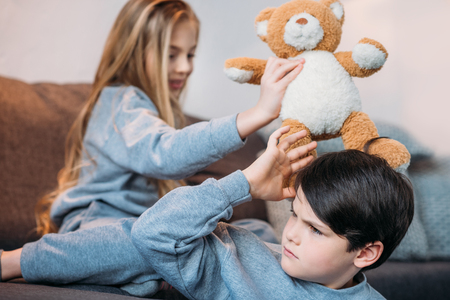 boy and girl playing with teddy bear and sitting on sofaの写真素材