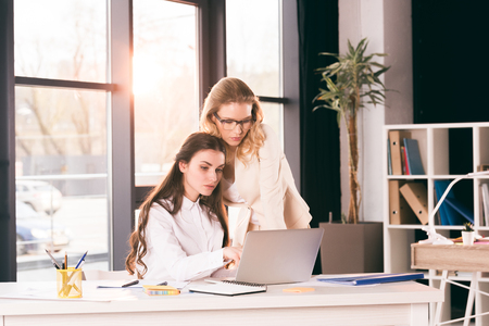 caucasian businesswomen in formalwear talking while working at modern officeの写真素材