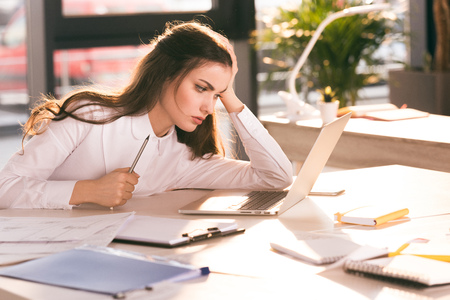 young businesswoman holding pencil and looking at laptop at workplaceの写真素材