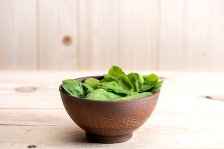 green spinach leaves in ceramic bowl on wooden tabletopの写真素材