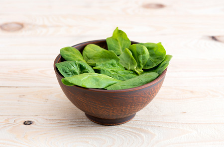 green spinach leaves in ceramic bowl on wooden tabletopの写真素材