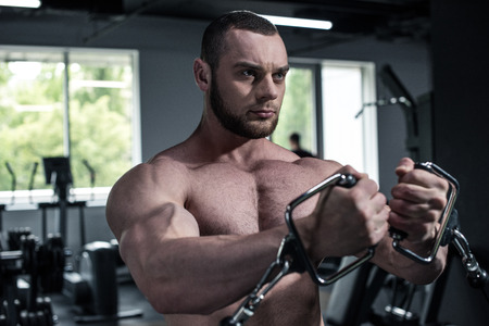 young shirtless bodybuilder training with weight machine at gym
