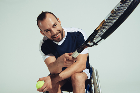 happy tennis player sitting in wheelchair and holding tennis racquet and ballの写真素材