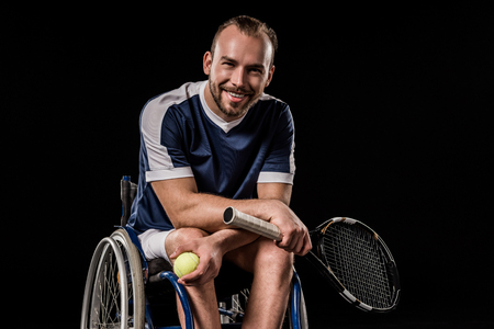 young man in sportswear sitting in wheelchair and holding tennis racquet with ballの写真素材