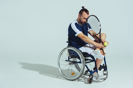 upset tennis player sitting in wheelchair and holding tennis racquet and ballの写真素材
