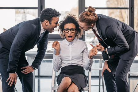 two emotional businessmen in formalwear screaming on businesswoman in office