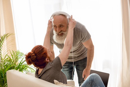 Mature woman with laptop adjusting headphones to bearded manの写真素材