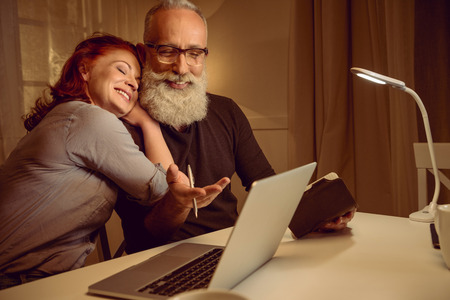smiling middle aged couple sitting at table near laptop at homeの写真素材
