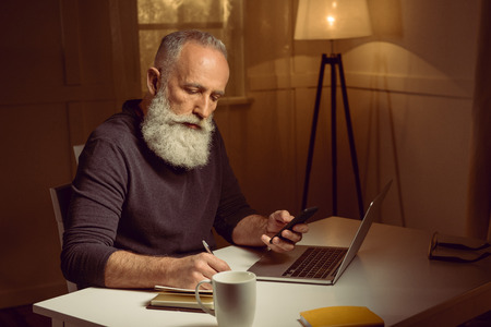 haired man working at home using digital devices and notebook