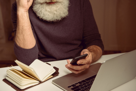 cropped shot of grey haired man sitting at table and using smartphone at homeの写真素材