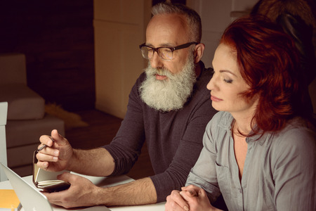 middle aged couple looking at laptop while sitting at tableの写真素材