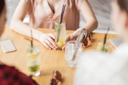 young girls drinking cocktails together while sitting at table in cafeの写真素材