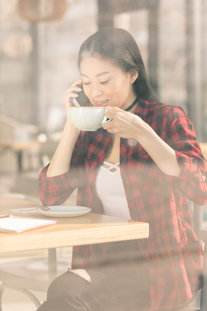 attractive asian girl using smartphone and drinking coffee in cafeの写真素材