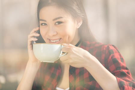 attractive asian girl using smartphone and drinking coffee in cafeの写真素材