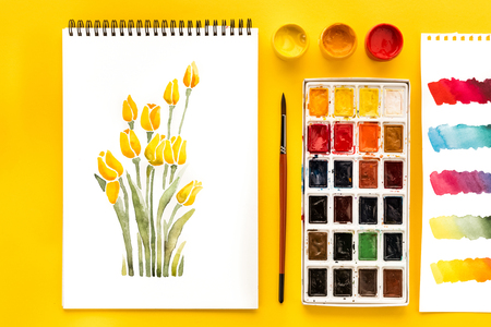 top view of drawing of flowers, paints, brush and colorful brushstrokes on paper on yellowの写真素材