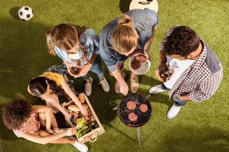 happy young friends grilling burgers and drinking beer at picnicの写真素材