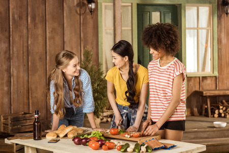 young women cutting fresh vegetables and smiling each other outdoorsの写真素材
